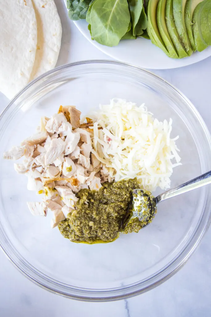 mixing chicken, pesto and cheese in a bowl