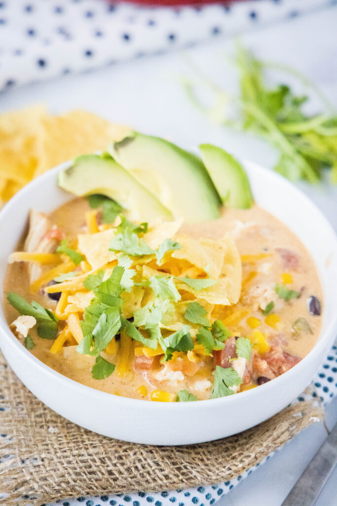 a bowl of chicken taco soup topped with cilantro, tortilla chips and avocado