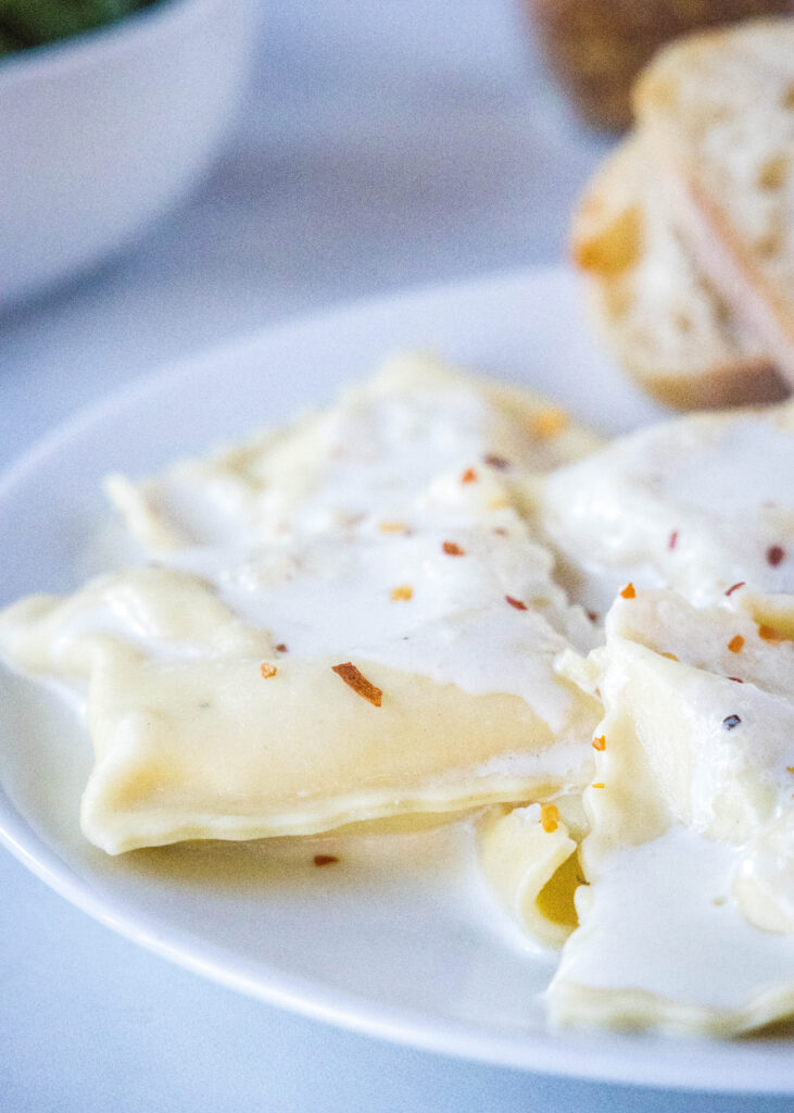 homemade ravioli with roasted garlic cream sauce on a white plate
