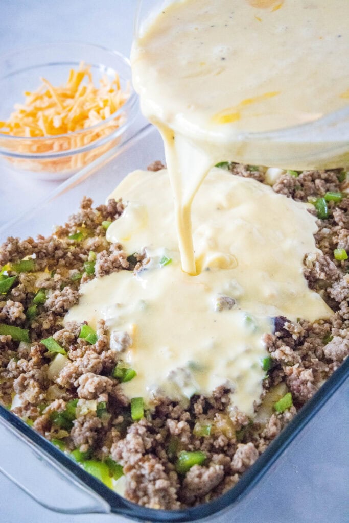 pouring egg mixture over sausage and green peppers in a baking dish