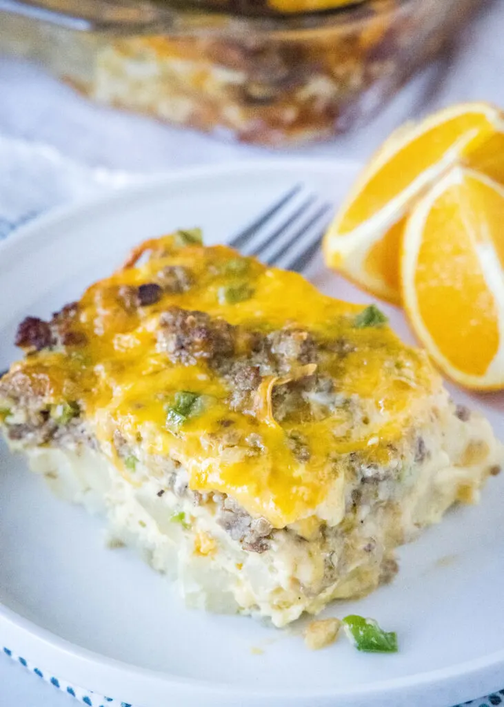 a white plate with a slice of sausage egg casserole and orange slices