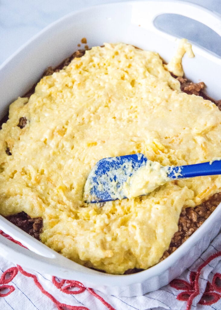 spreading cornbread batter over sloppy joes