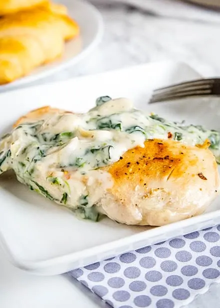 a white plate with spinach and artichoke sauce over chicken