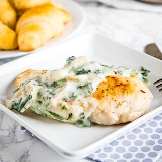 close up white plate with chicken topped with spinach and artichoke sauce