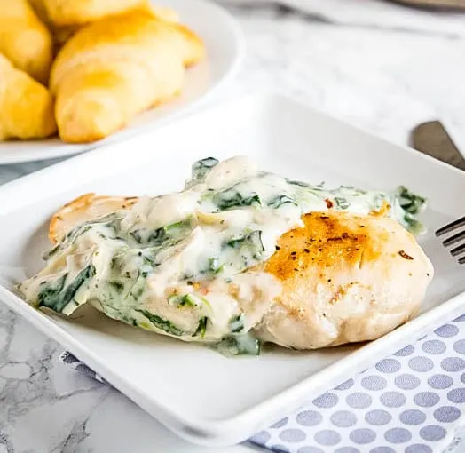 close up white plate with chicken topped with spinach and artichoke sauce