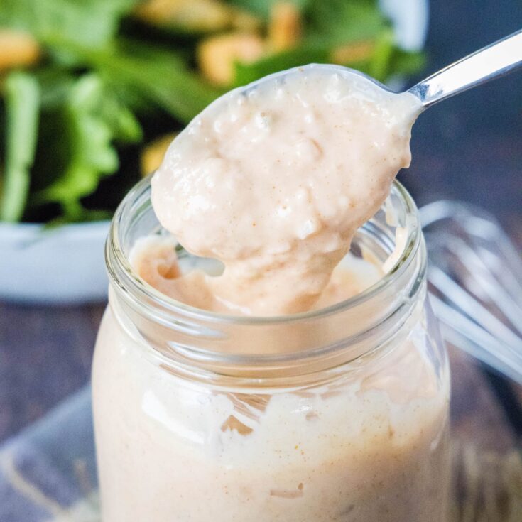 Cropped close up of salad dressing with a spoon from a jar
