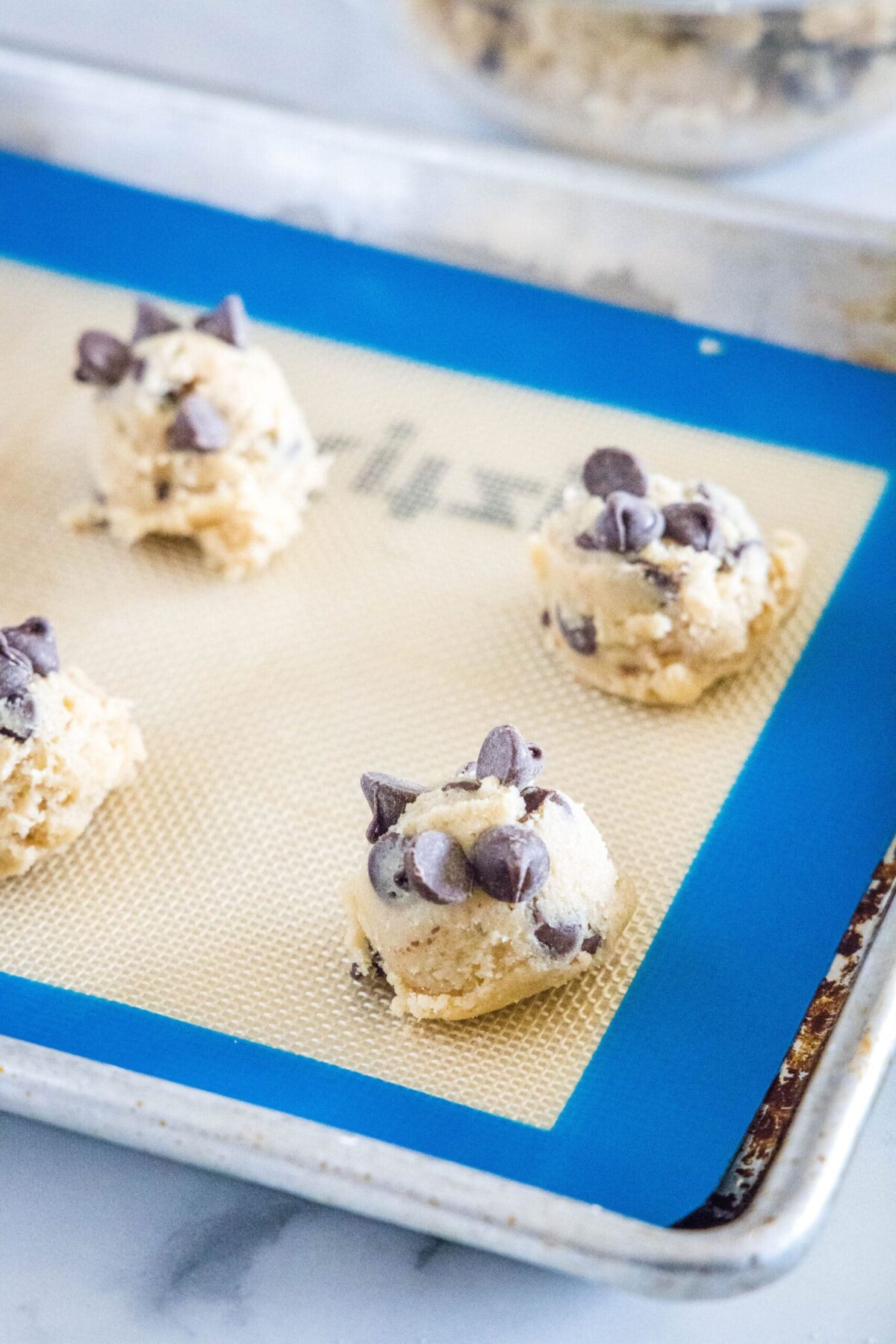 Raw chocolate chip cookie dough balls on a silicone mat on a baking sheet