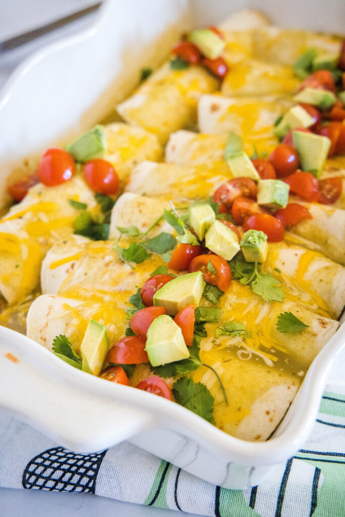 breakfast enchiladas topped with avocado, and tomatoes in a baking dish