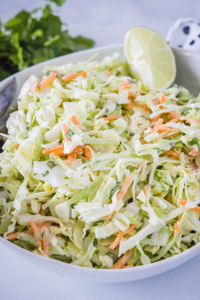 creamy mexican coleslaw in a white bowl with a slice of lime