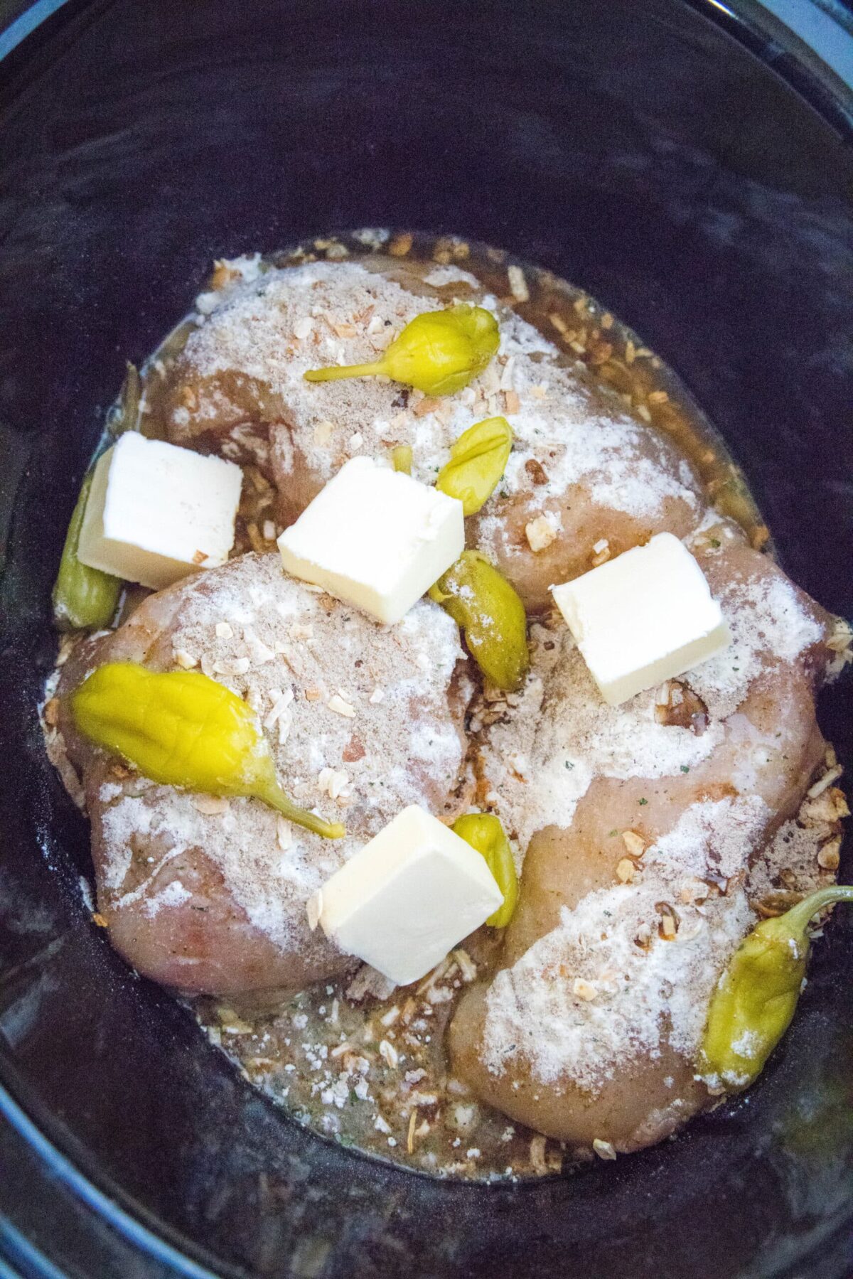 Poitrines de poulet crues dans une mijoteuse avec des piments pepperoncini, des morceaux de beurre, un mélange de vinaigrette ranch, un mélange de soupe à l'oignon et du jus de pepperoncini