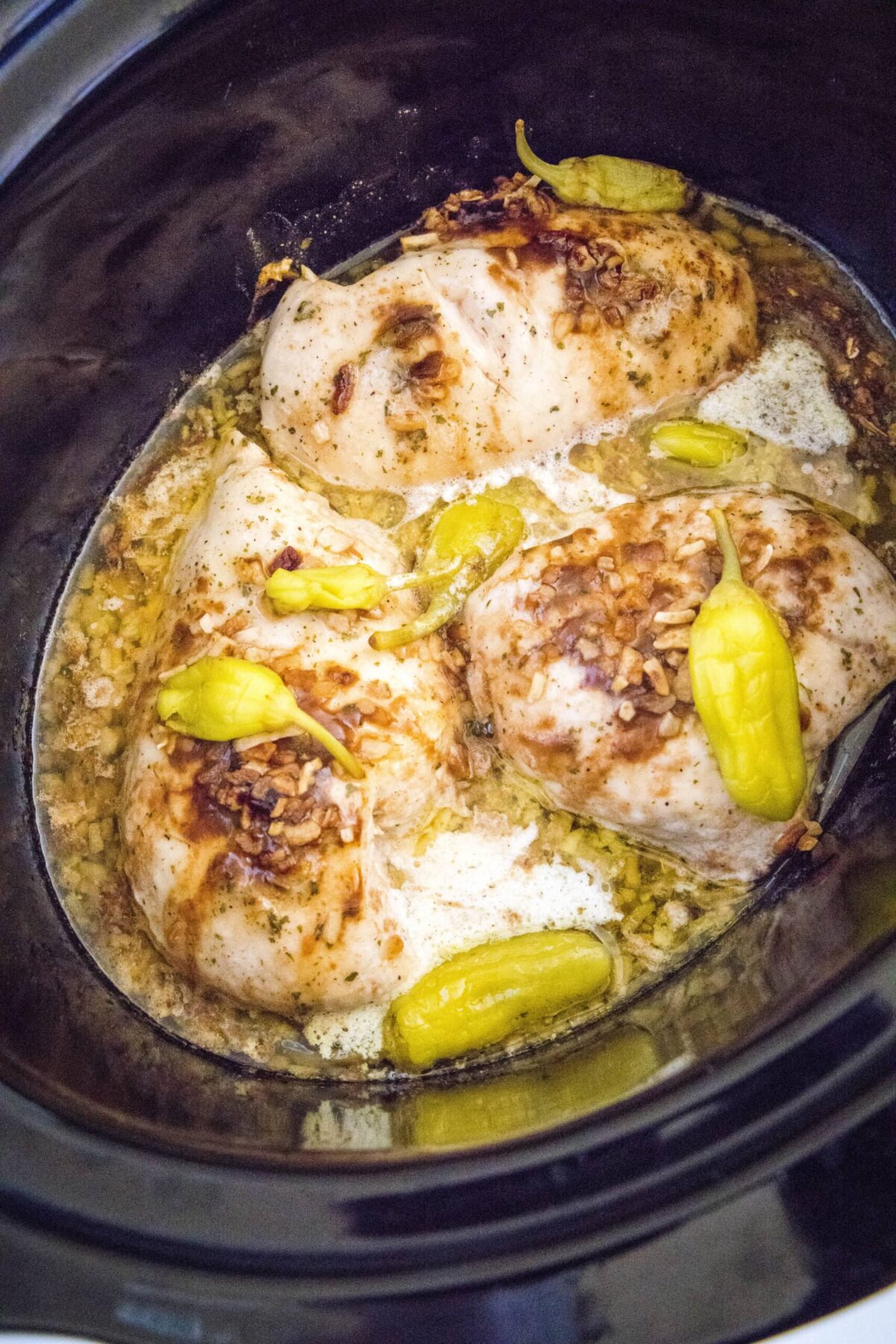 Cooked chicken breasts in a slow cooked with liquid and pepperoncini pepper