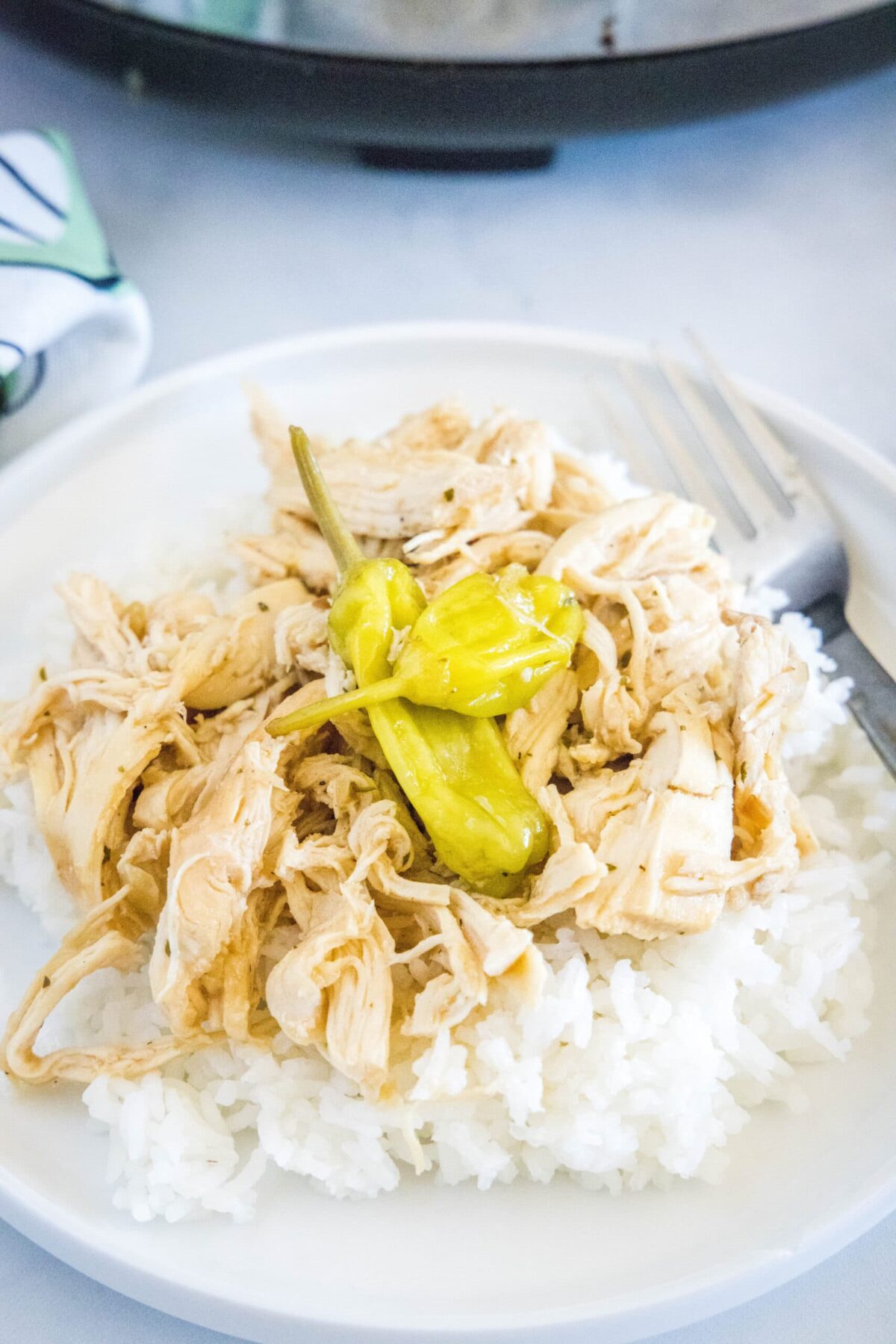 A plate with a fork and a bed of rice, topped with shredded chicken and pepperoncini peppers