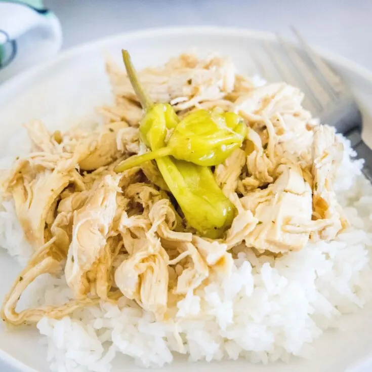 A plate with shredded chicken on top of rice, topped with pepperoncini peppers, with a fork on the plate