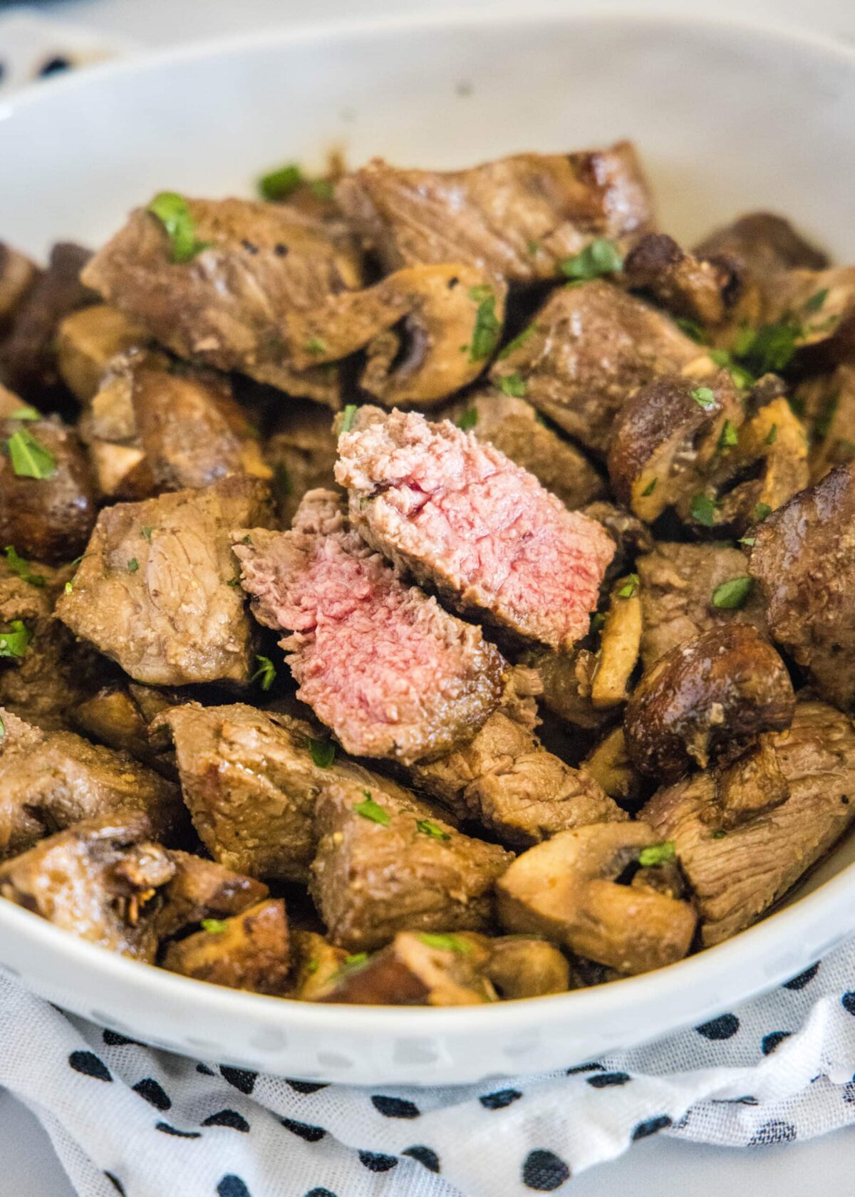 A serving bowl full of steak and mushroom bites, with one of the pieces of steak cut in half
