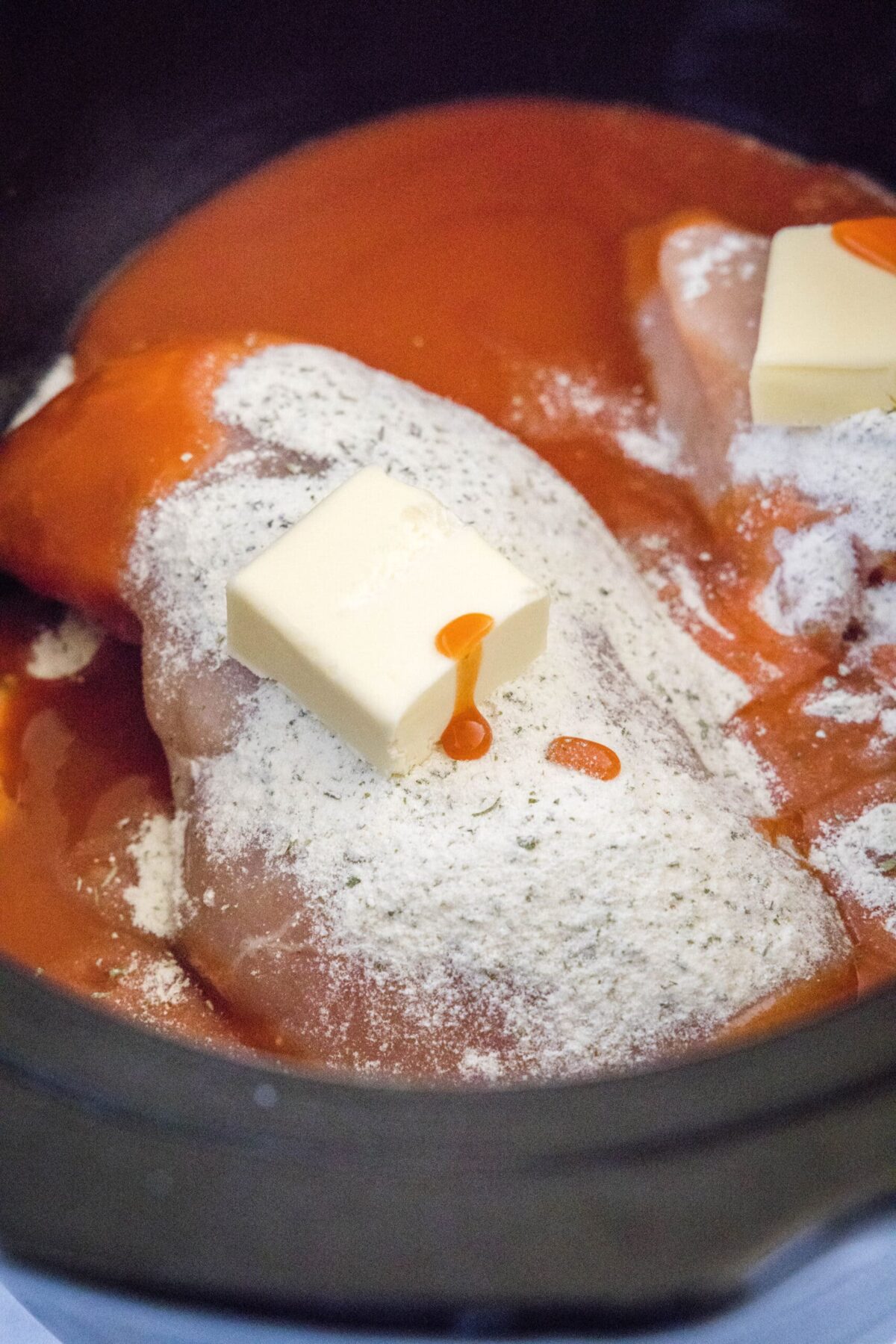 Chicken breasts in a slow cooker topped with ranch dressing mix, buffalo sauce, and butter