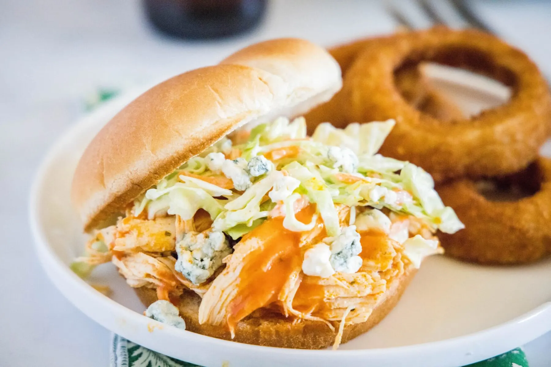 A plate with a buffalo chicken sandwich and onion rings on it
