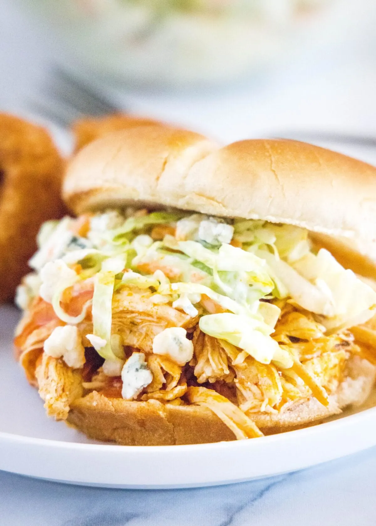 Close up of a buffalo chicken sandwich topped with coleslaw and blue cheese
