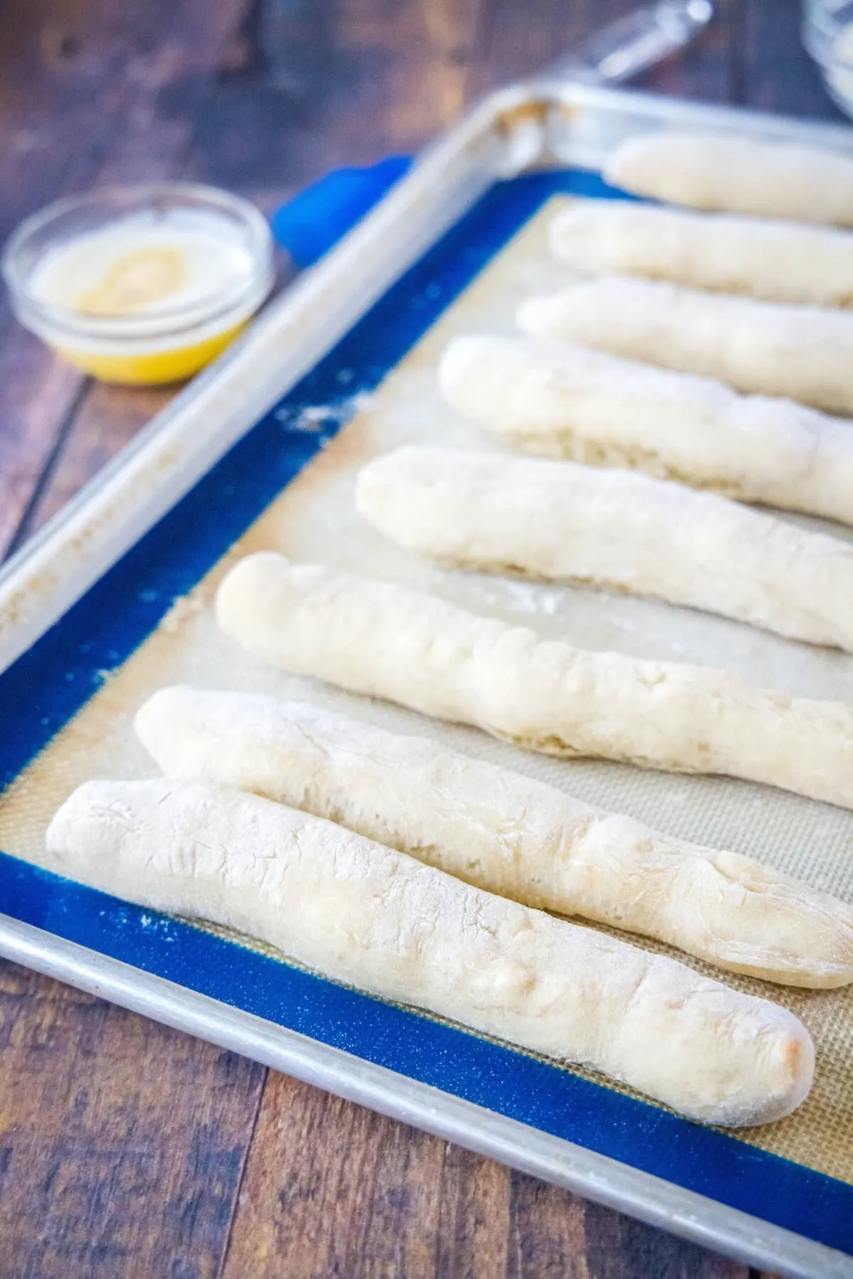 Baked breadsticks sitting on a baking sheet with a bowl of butter behind them