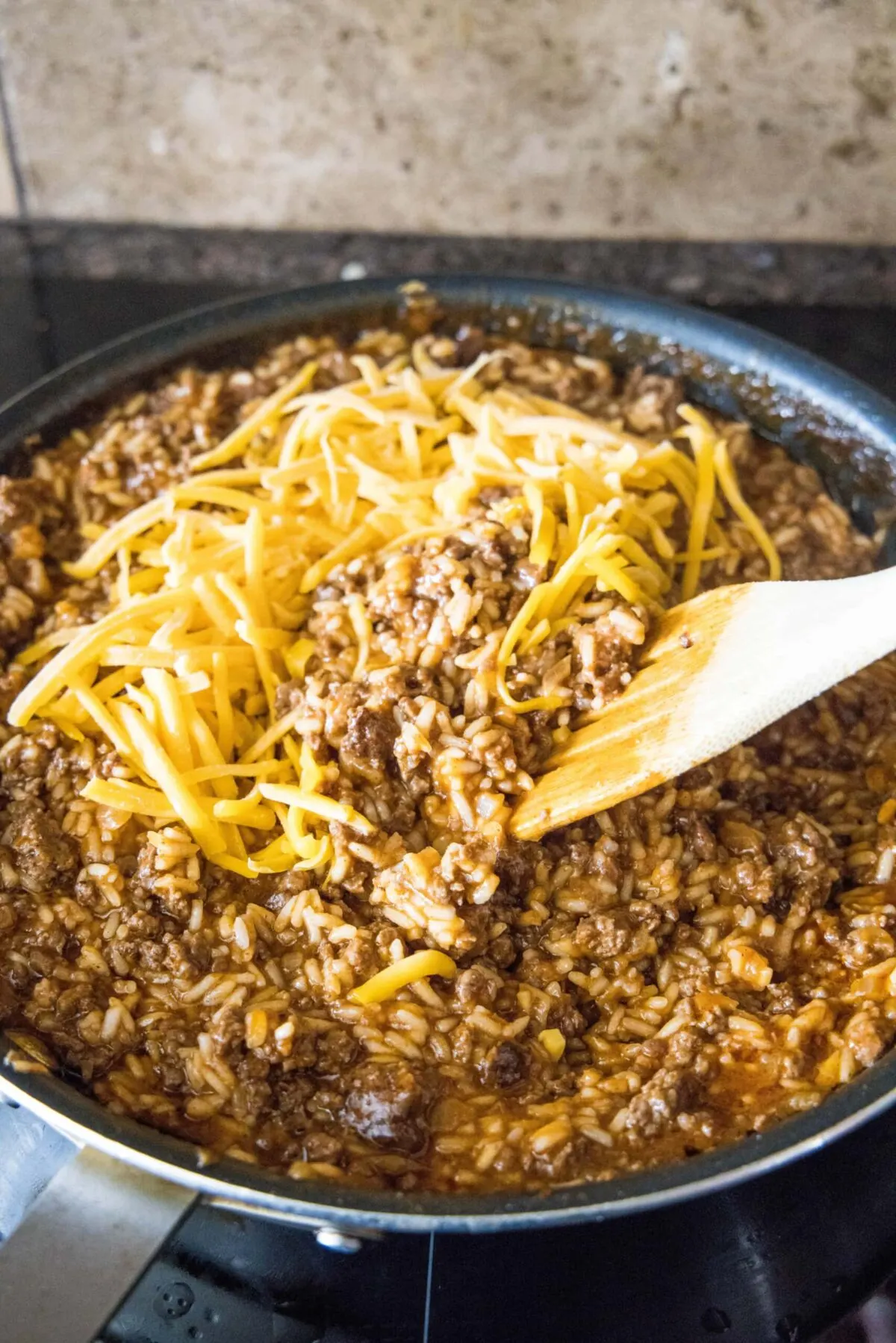 A wooden spoon stirring shredded cheese into beefy rice
