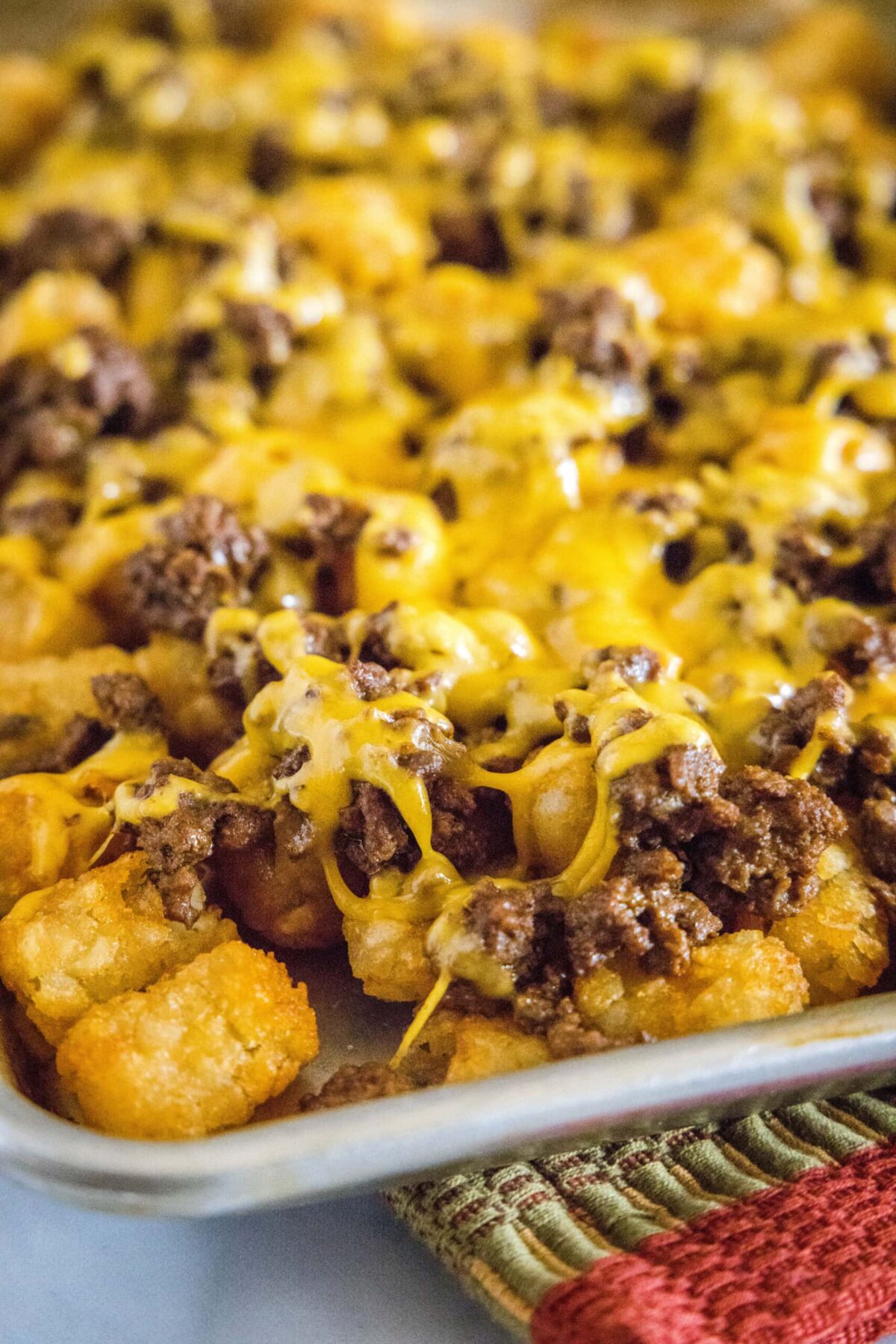 Close up of cheese melted over ground beef and tater tots on a baking sheet
