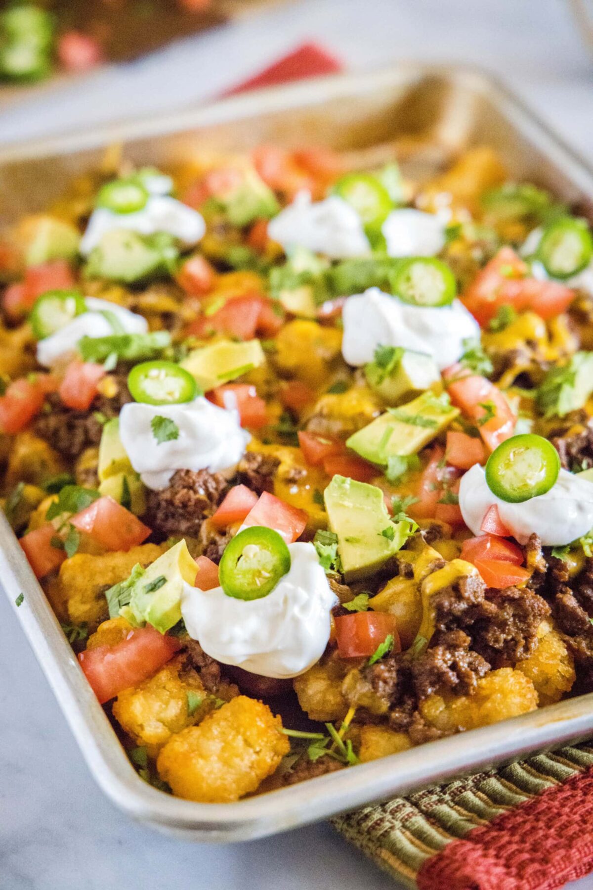 A baking sheet of tater tot nachos topped with tomatoes, sour cream, jalapeños, avocado, and cilantro