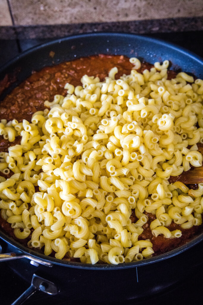 Cooked elbow macaroni in a skillet on top of sauce.