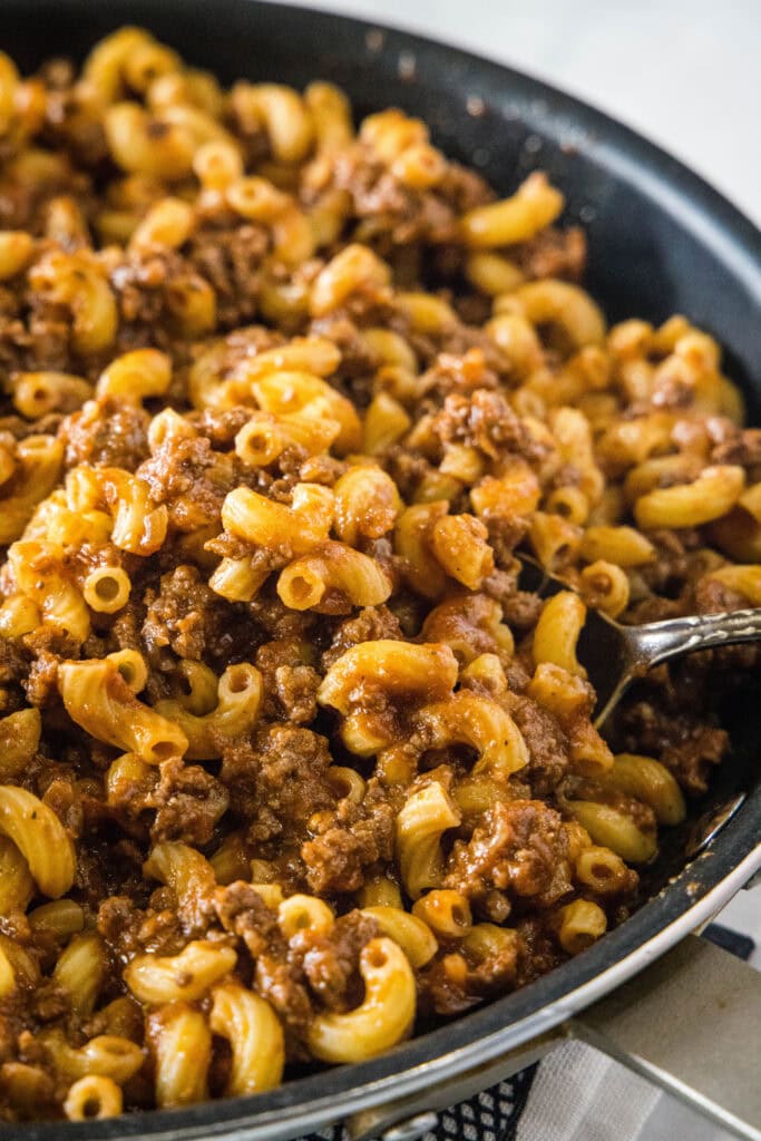 Beefaroni in a skillet, with a spoon lifting out a bite.