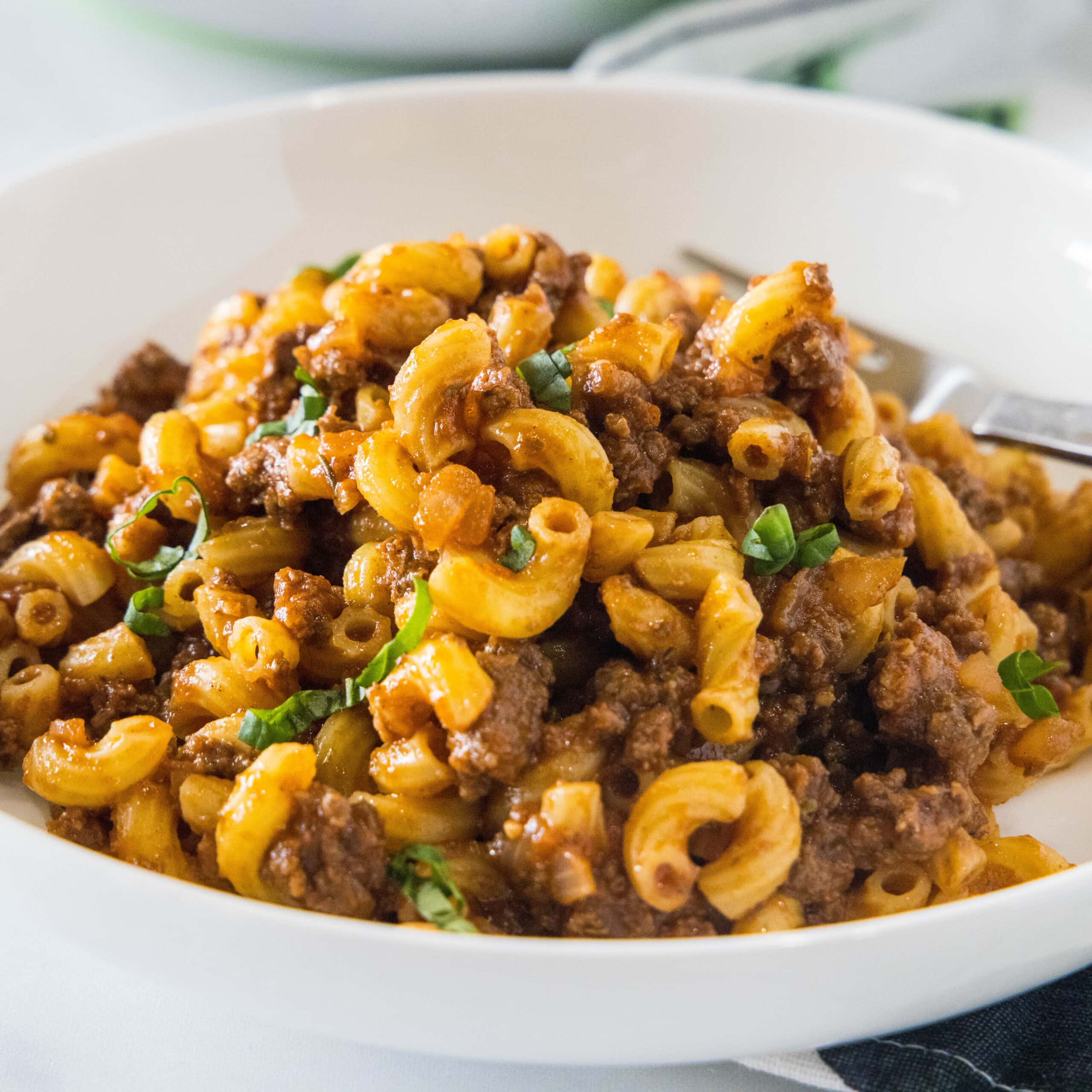 A white bowl with beefaroni and a fork