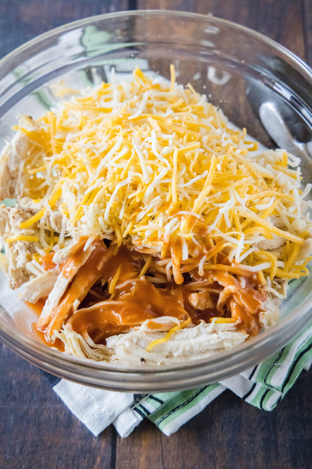 A mixing bowl filled with shredded chicken, wing sauce, and shredded cheese