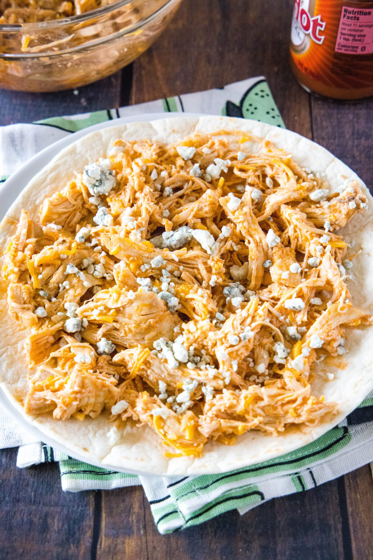 A plate with a tortilla topped with buffalo chicken and cheese mixture, topped with blue cheese crumbles