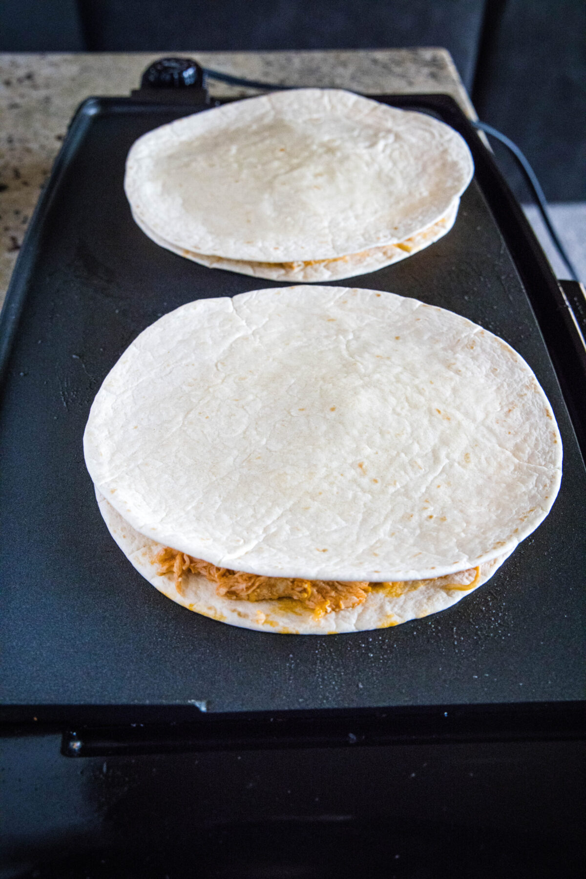 Two uncooked quesadillas on a skillet