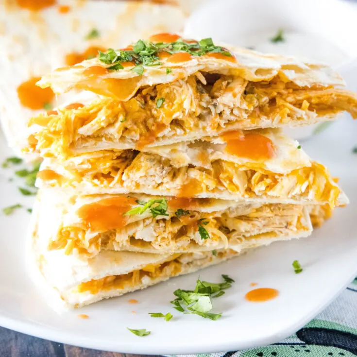 A stack of slices of buffalo chicken quesadillas on a plate, topped with cilantro