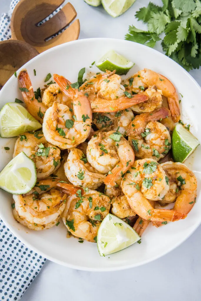 cilantro lime shrimp in a white bowl with wedges of lime
