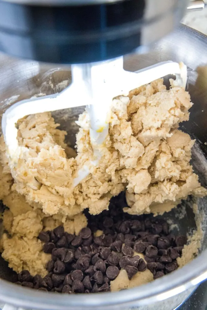 A stand mixer paddle mixing cookie dough with a pile of chocolate chips