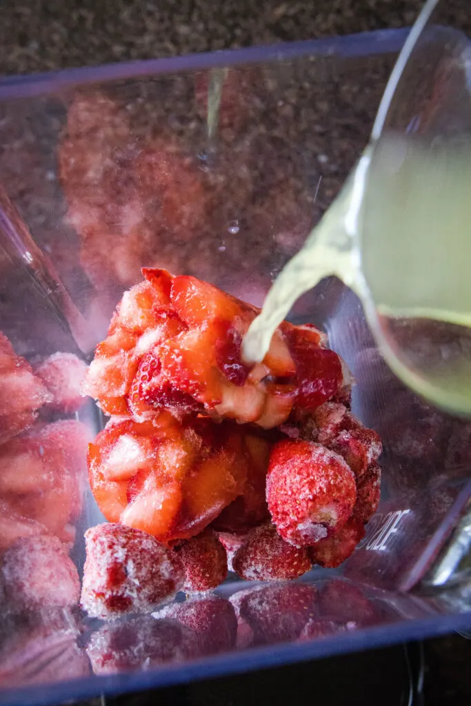 frozen strawberries in a blender pouring lemonade over it