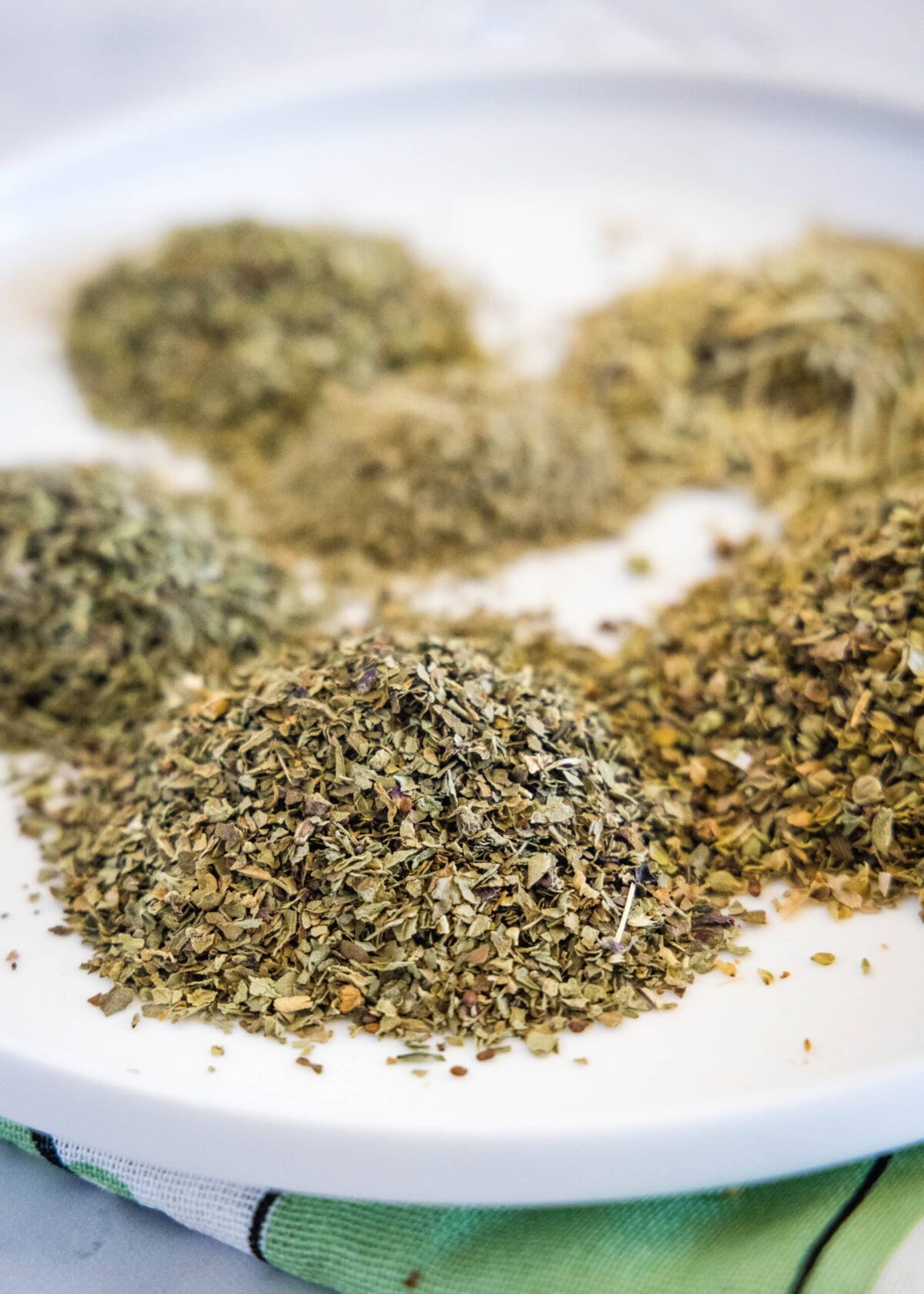 Close up view of a plate with piles of dried basil, oregano, marjoram, thyme, rosemary, and sage