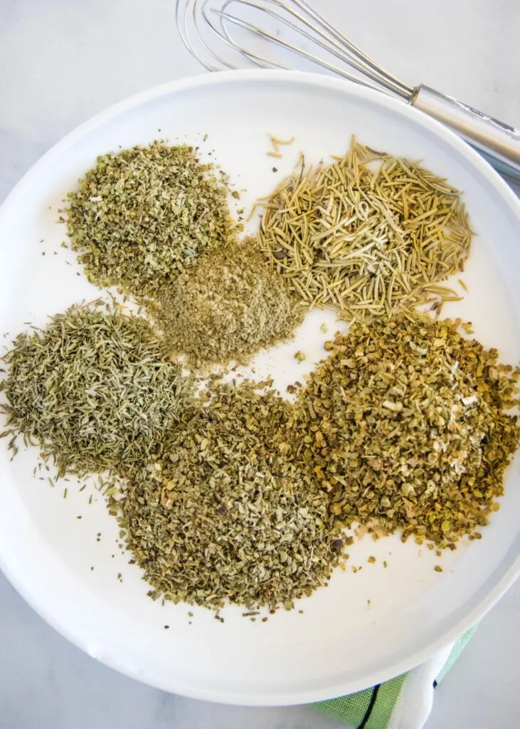 Piles of dried basil, thyme, oregano, marjoram, rosemary, and sage on a plate