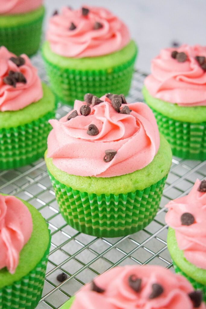 cooling rack with green cupcakes topped with pink frosting