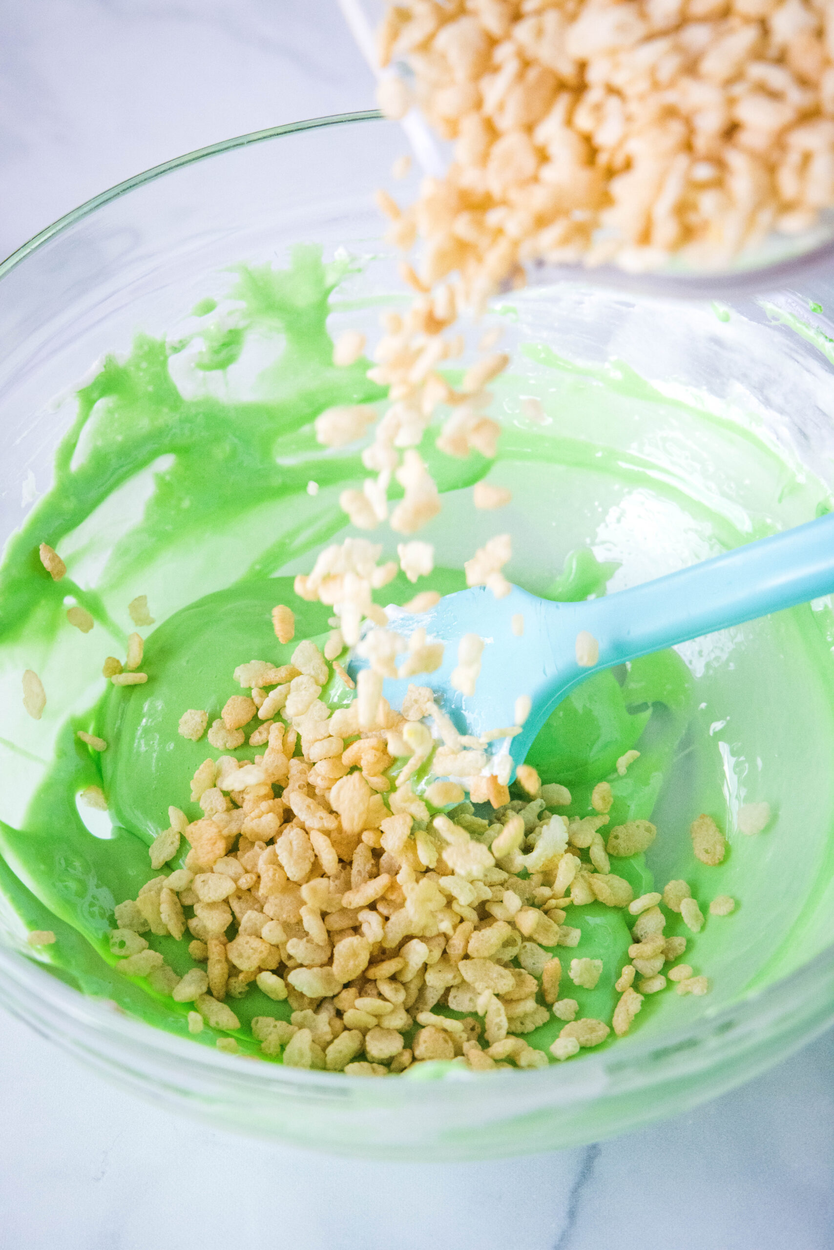 adding krispies to melted green marshmallos