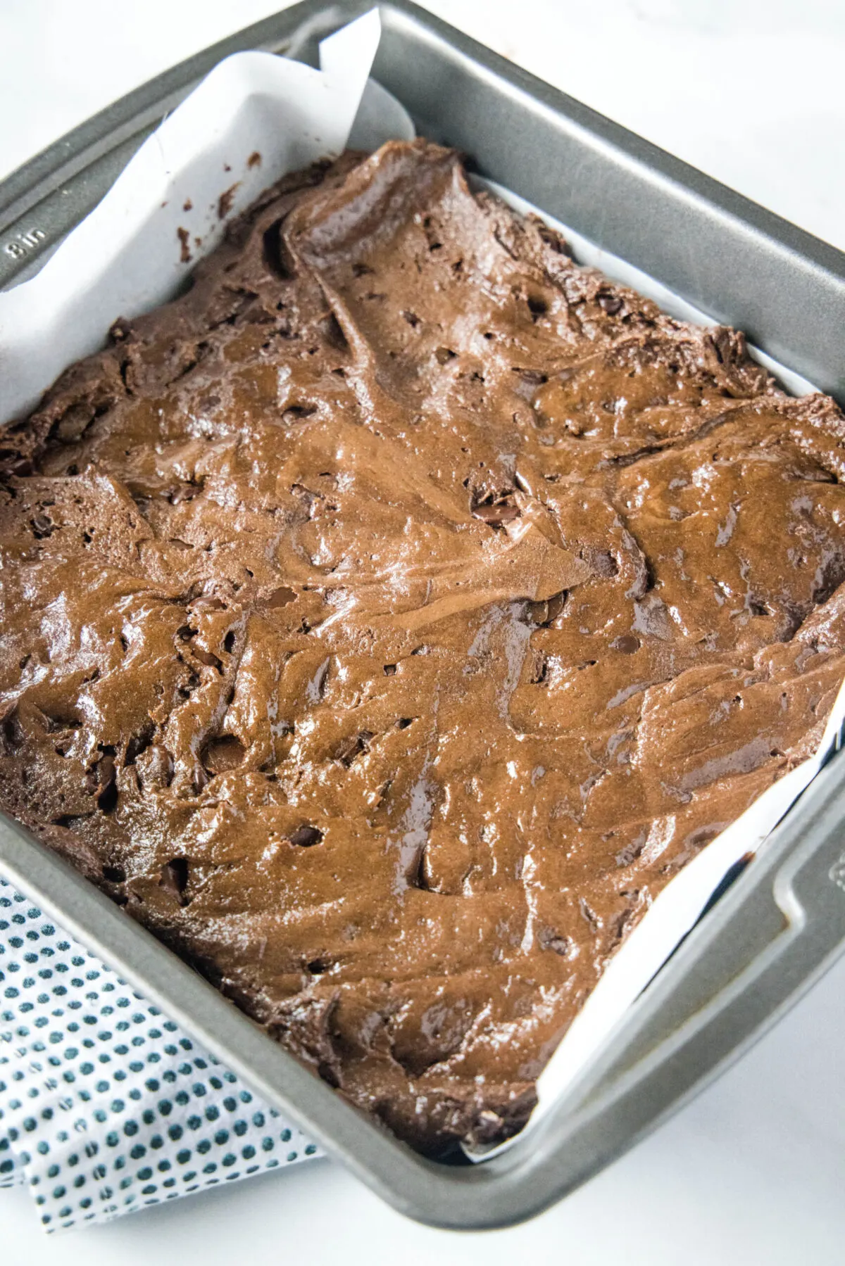 Overhead view of a square baking dish lined with parchment paper and filled with brownie batter