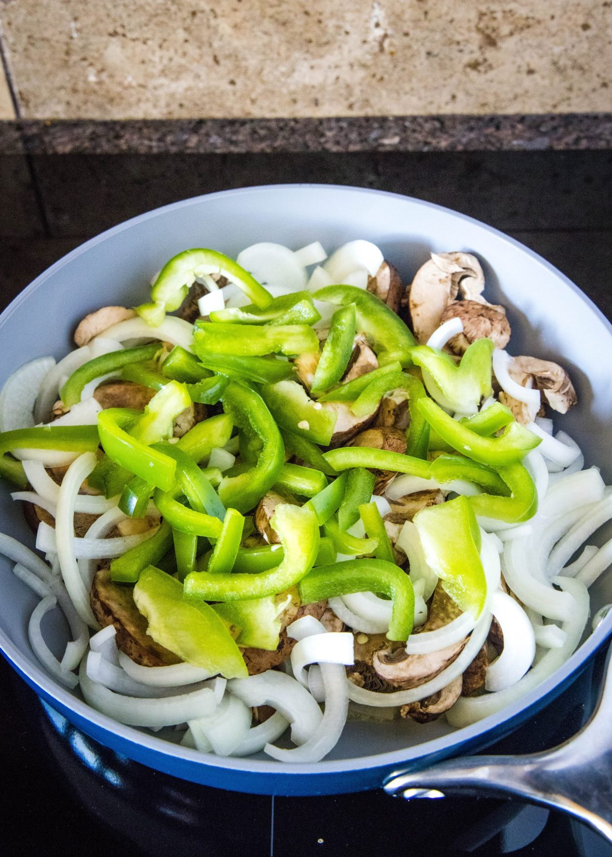 A skillet full of uncooked mushrooms, onions, and green bell pepper
