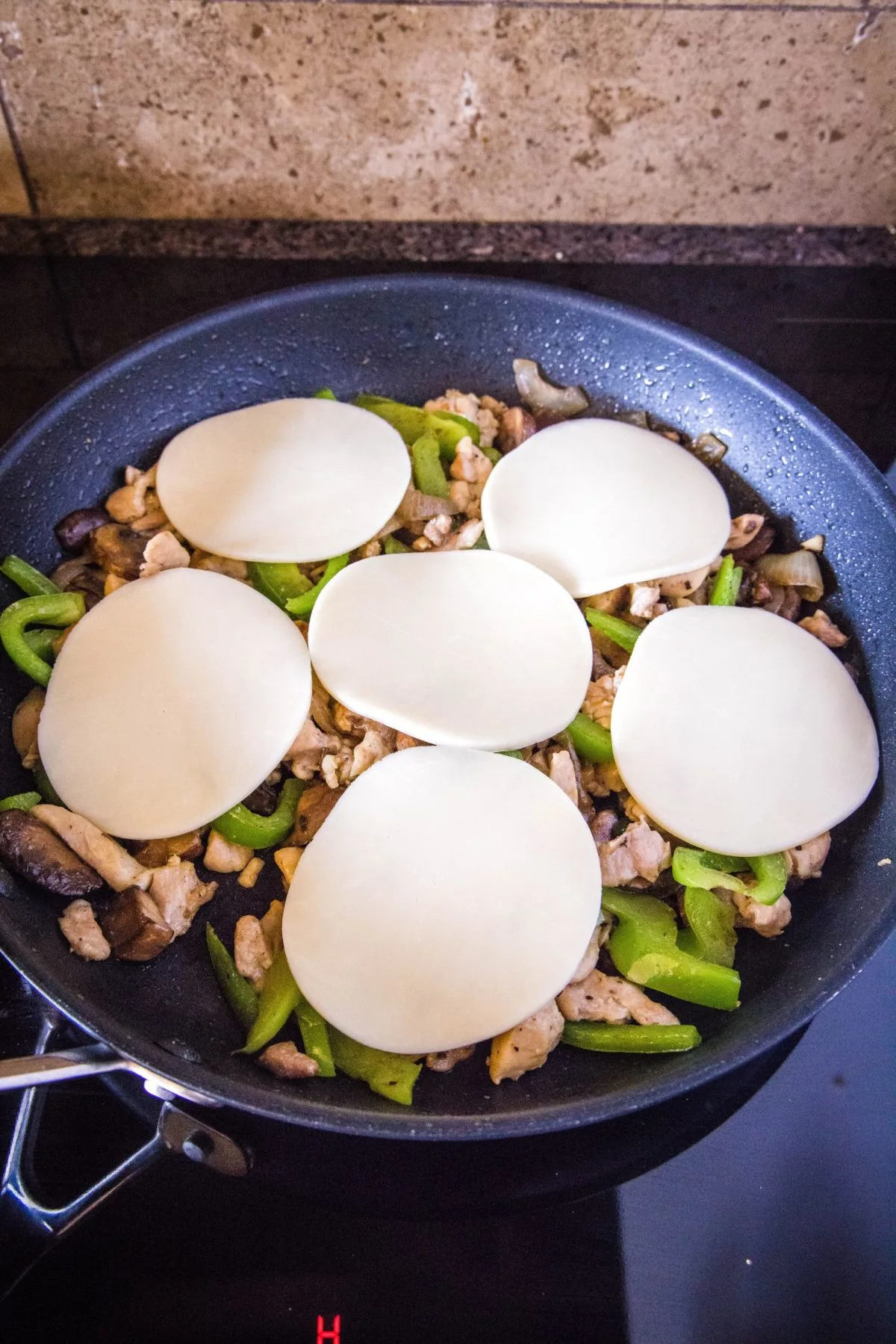 Slices of provolone cheese on top of onions, peppers, mushrooms, and chicken in a skillet