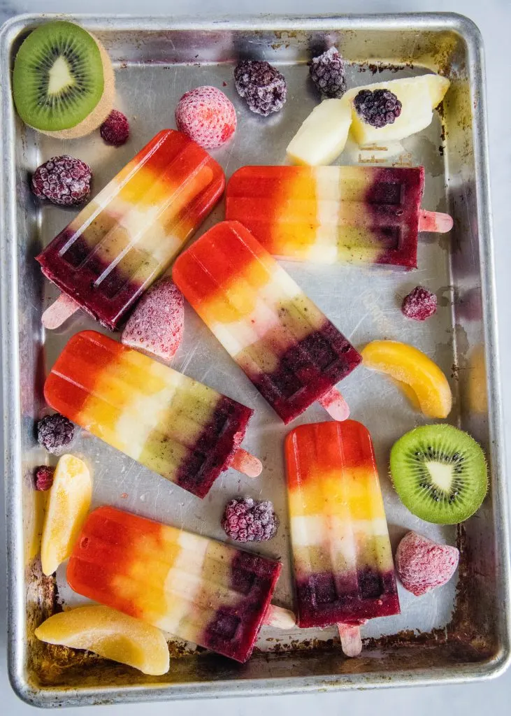 Rainbow popsicles on a baking sheet with frozen fruit