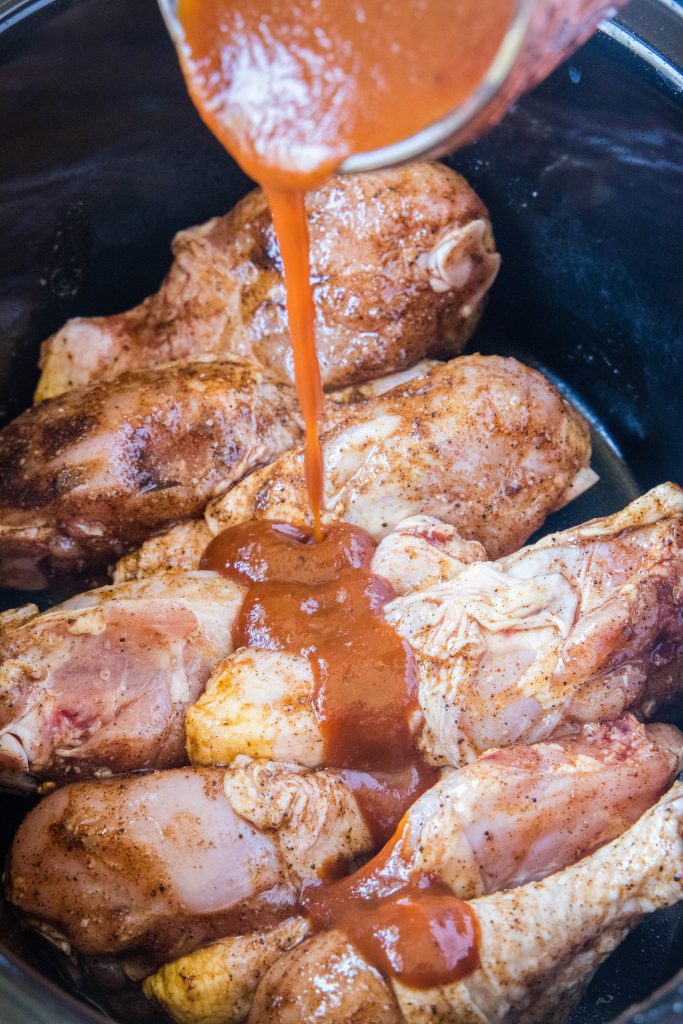 pouring barbecue sauce over drumsticks in crockpot