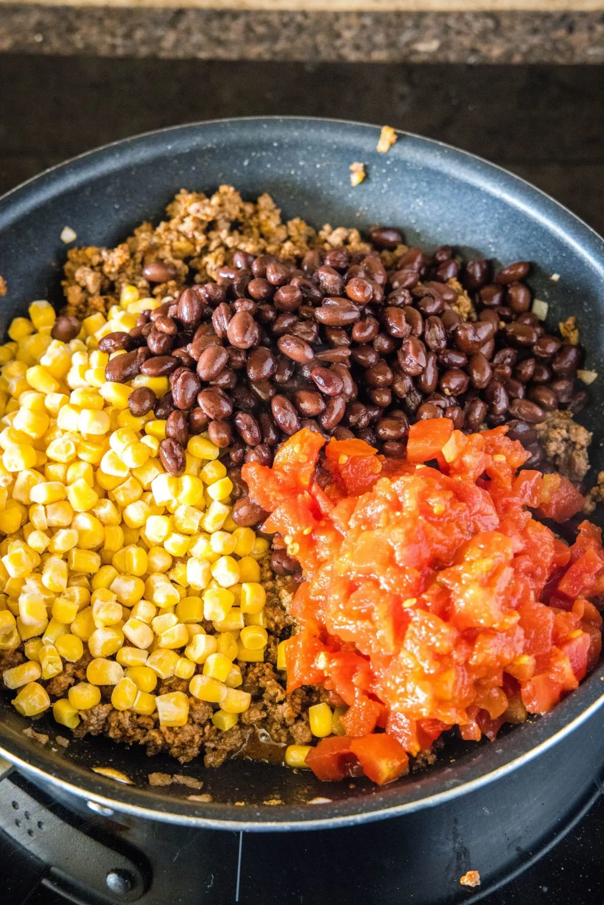 Corn, black beans, and salsa in a skillet on top of ground beef and onions