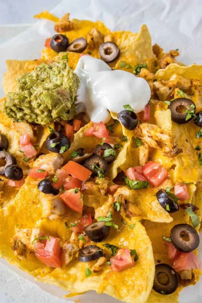 chicken nachos on paper topped with gaucamole and sour cream