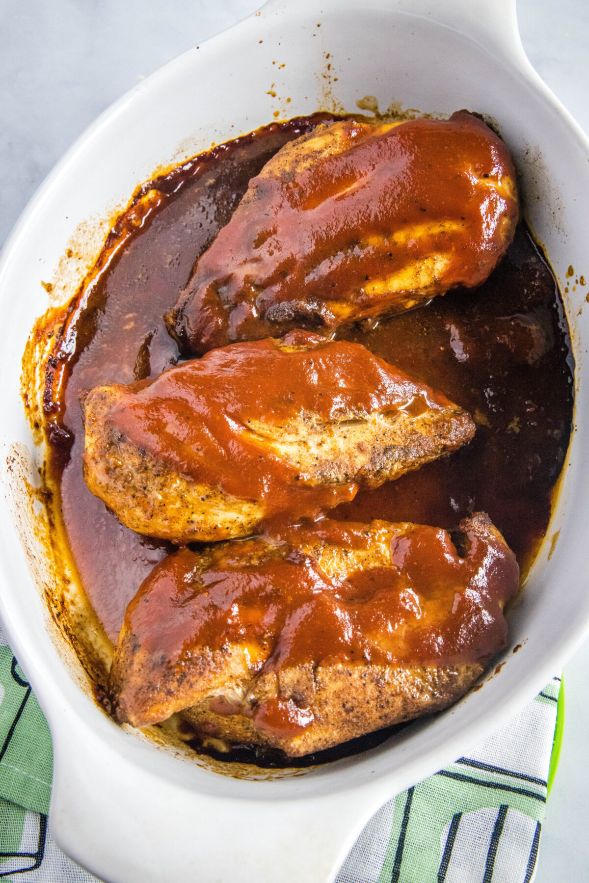 Overhead view of three chicken breasts in a pot full of BBQ sauce, covered in BBQ sauce