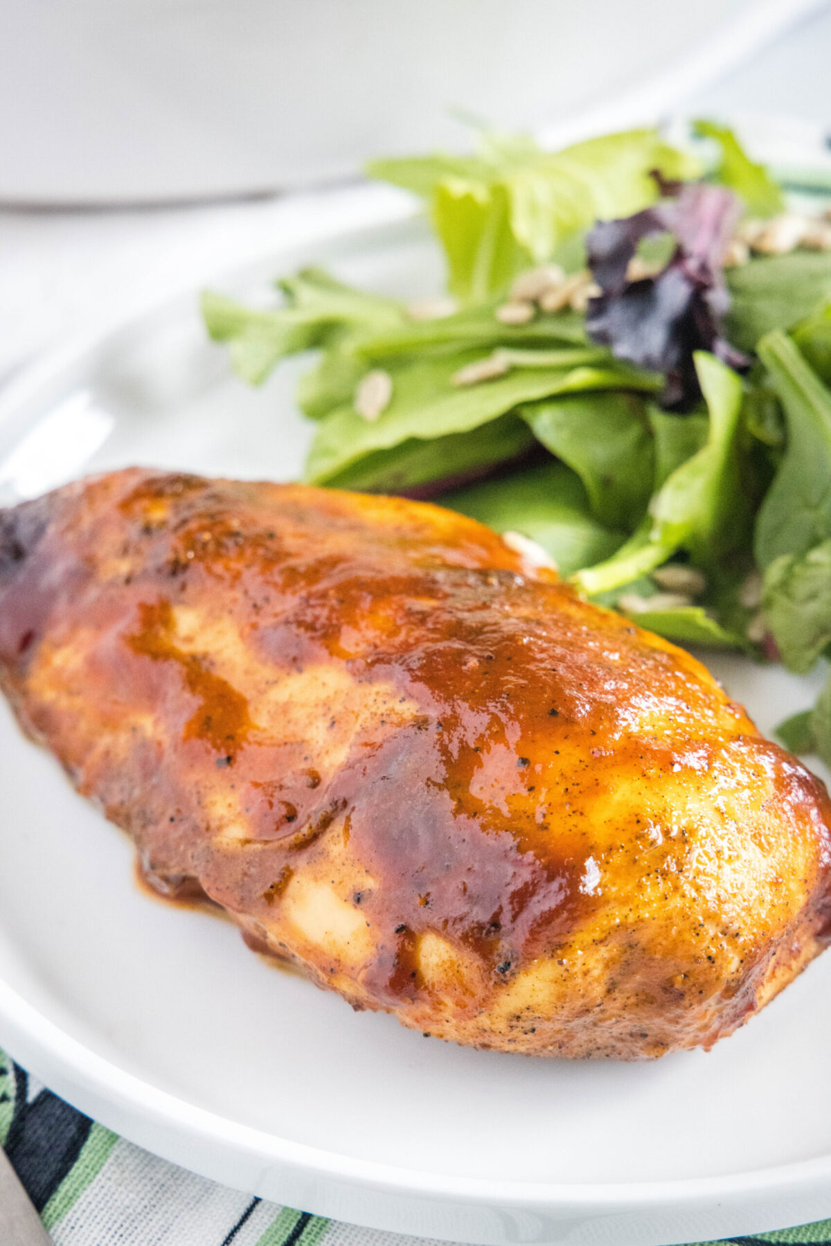 A BBQ chicken breast on a plate with salad