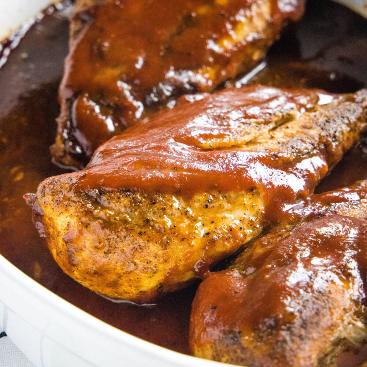 Three chicken breasts covered in BBQ sauce, in a pot