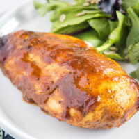 Close up picture of a BBQ chicken breast on a plate next to some salad